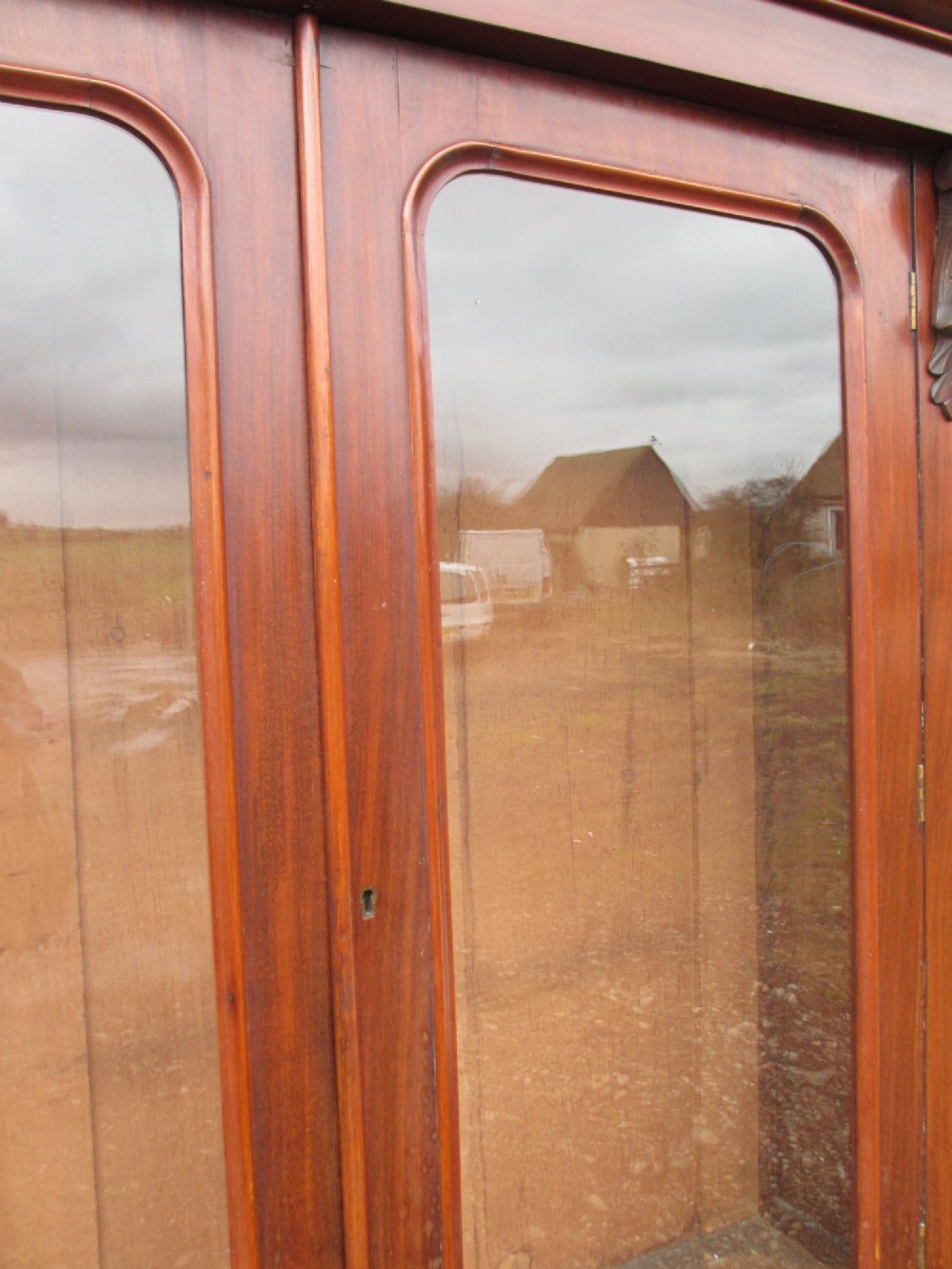 A two-piece Victorian mahogany bookcase featuring an upper section with two glazed doors and carved corbels over a lower cabinet with flame mahogany panelled doors. View VI