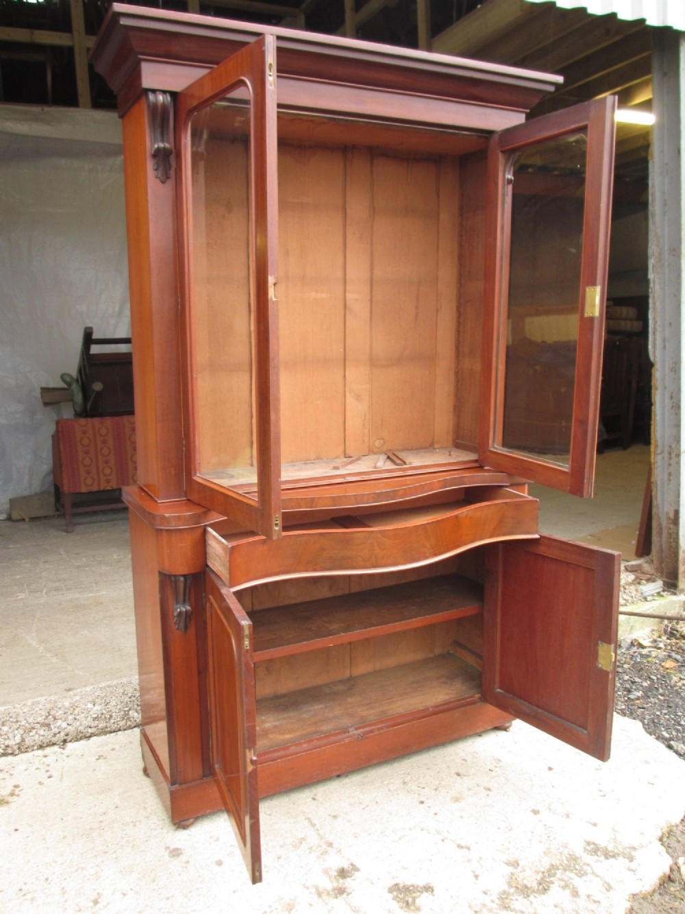 A two-piece Victorian mahogany bookcase featuring an upper section with two glazed doors and carved corbels over a lower cabinet with flame mahogany panelled doors. View XI