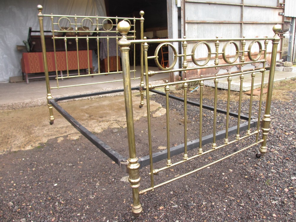 A Victorian brass bed frame featuring circular motifs, vertical spindles, ball finials, and an iron slot frame set on castors. View III