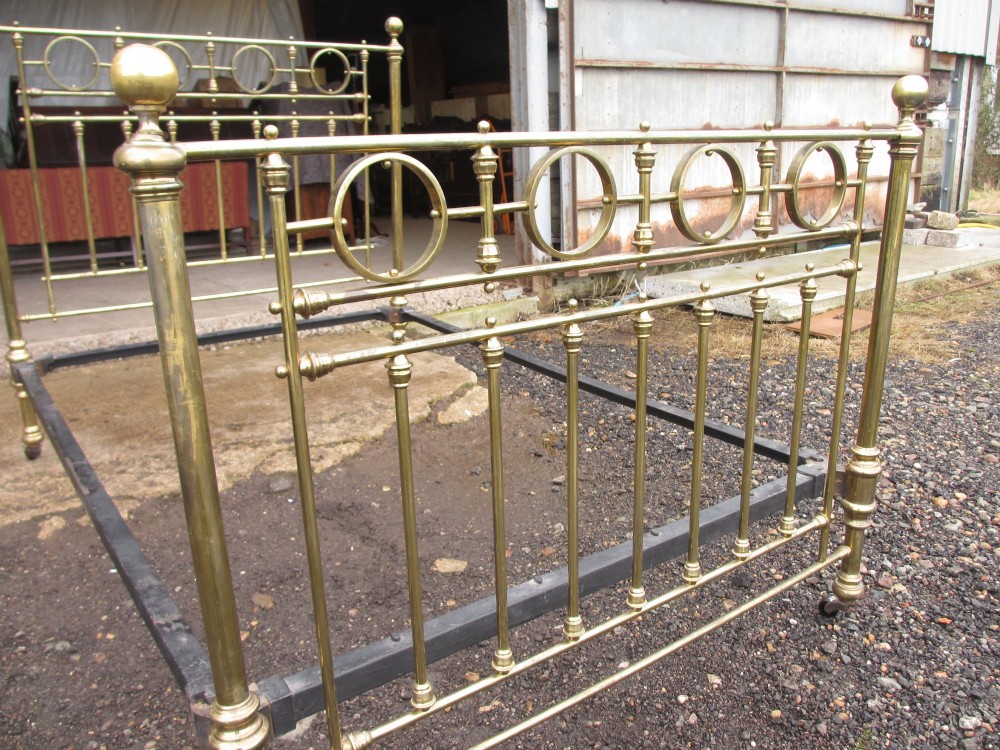 A Victorian brass bed frame featuring circular motifs, vertical spindles, ball finials, and an iron slot frame set on castors. View IV