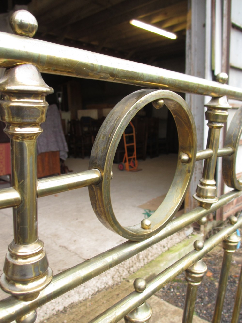 A Victorian brass bed frame featuring circular motifs, vertical spindles, ball finials, and an iron slot frame set on castors. View VII