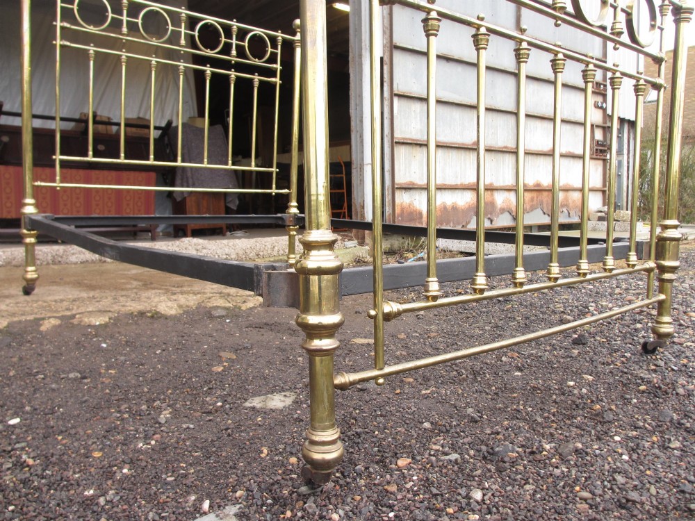 A Victorian brass bed frame featuring circular motifs, vertical spindles, ball finials, and an iron slot frame set on castors. View IX