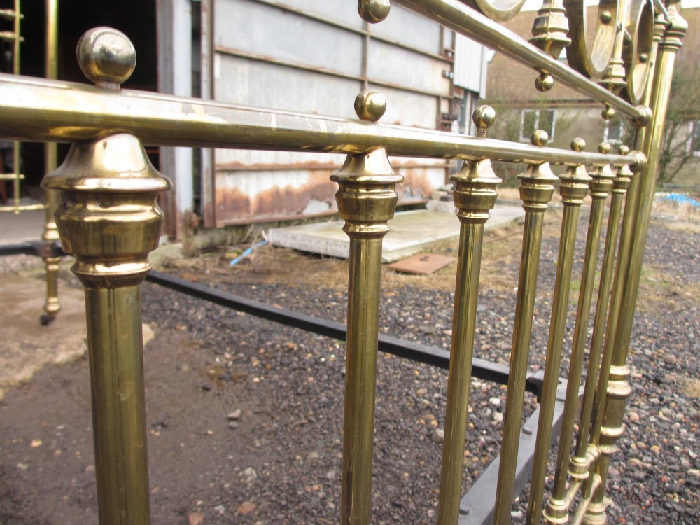 A Victorian brass bed frame featuring circular motifs, vertical spindles, ball finials, and an iron slot frame set on castors. View XI