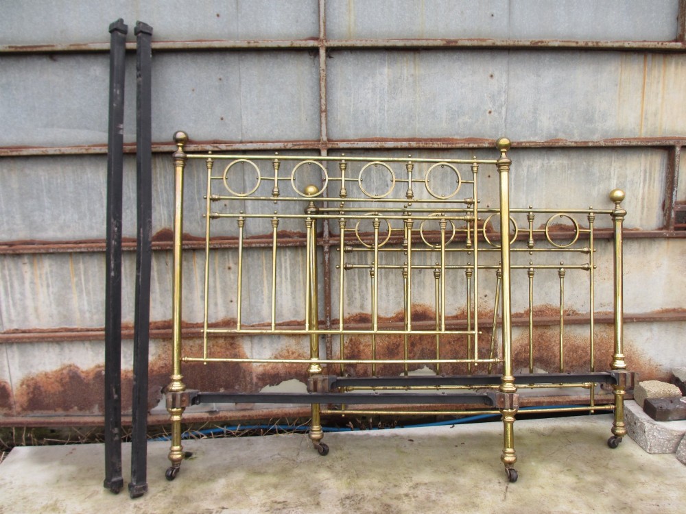A Victorian brass bed frame featuring circular motifs, vertical spindles, ball finials, and an iron slot frame set on castors. View XII