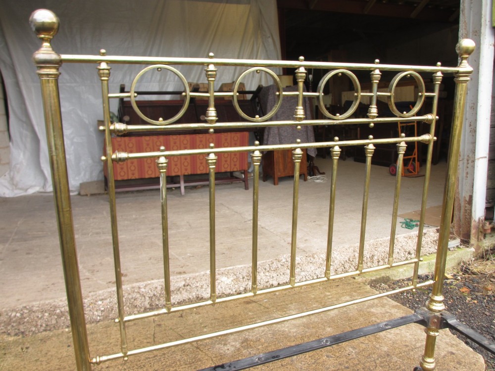 A Victorian brass bed frame featuring circular motifs, vertical spindles, ball finials, and an iron slot frame set on castors. View XIII