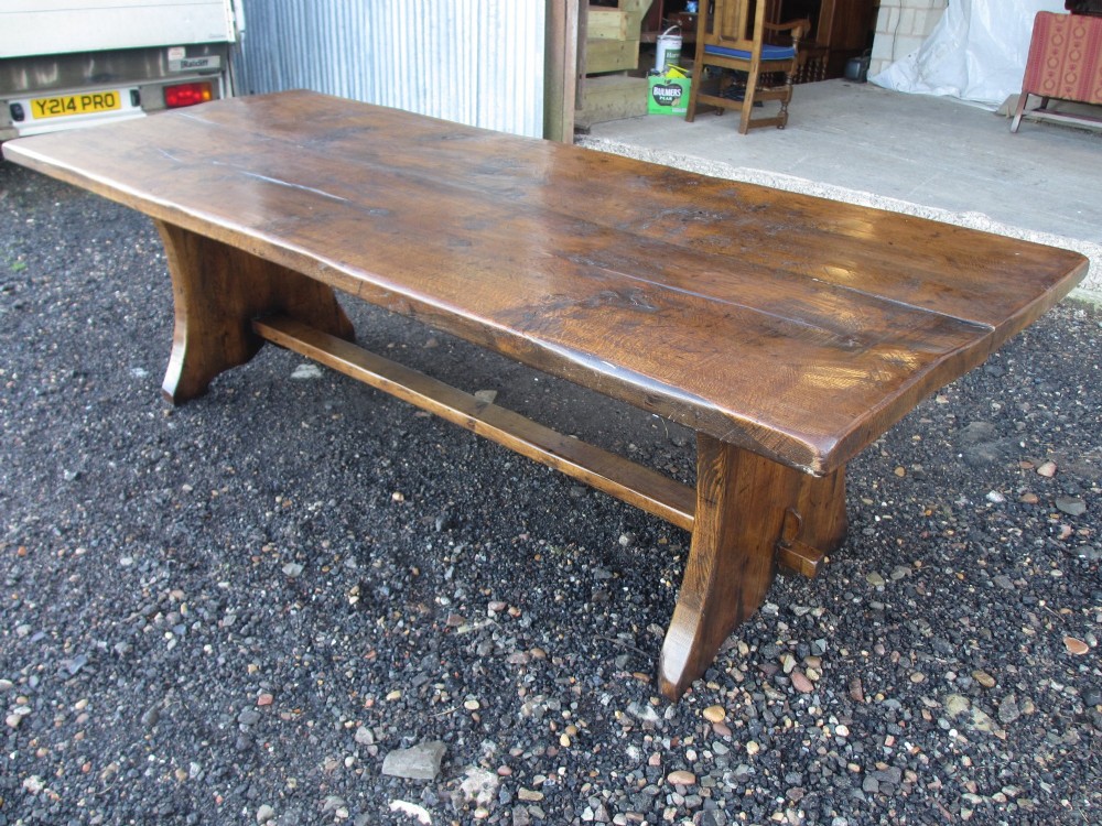 A solid oak refectory dining table with heavy trestle ends, accompanied by matching long wooden bench forms. View X