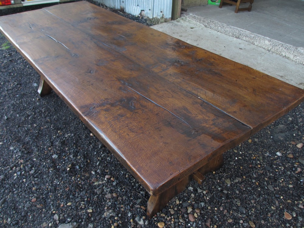 A solid oak refectory dining table with heavy trestle ends, accompanied by matching long wooden bench forms. View XI