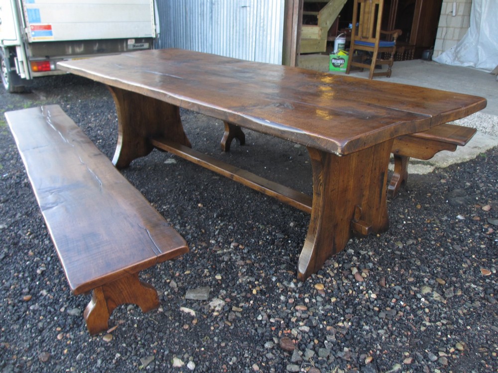 A solid oak refectory dining table with heavy trestle ends, accompanied by matching long wooden bench forms. View XIV