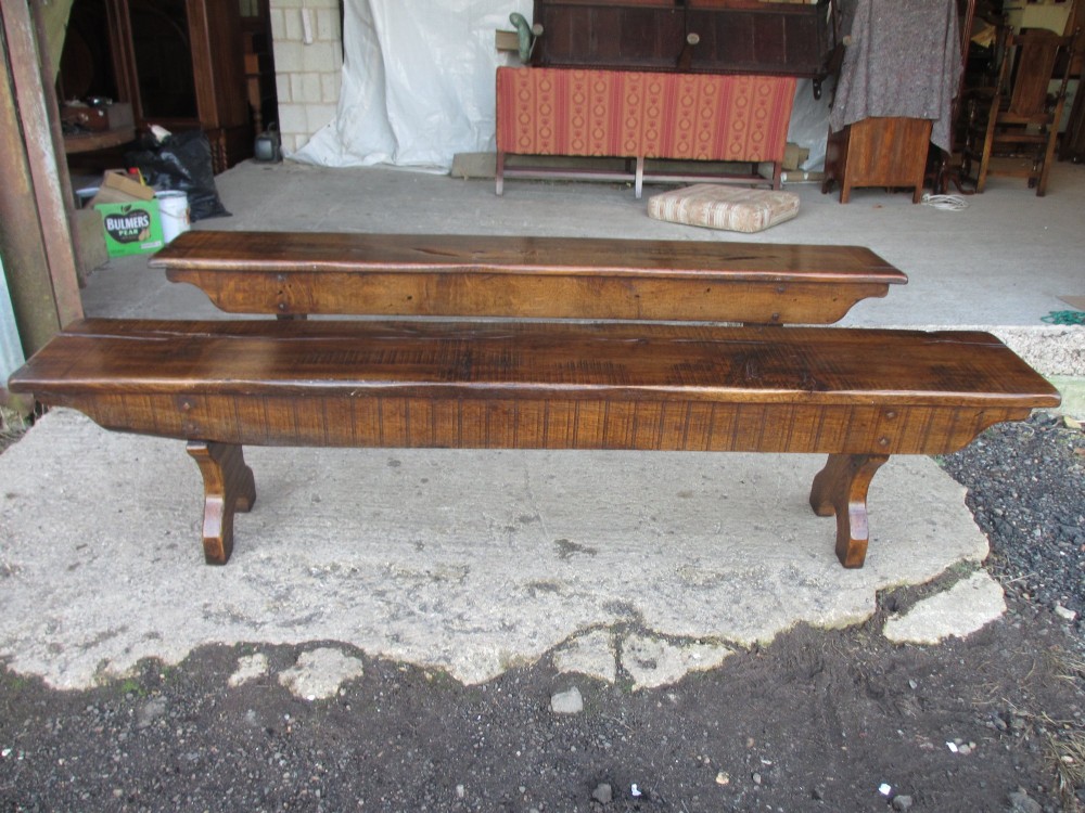 A long Edwardian solid oak bench featuring a rectangular seat and shaped trestle end supports.