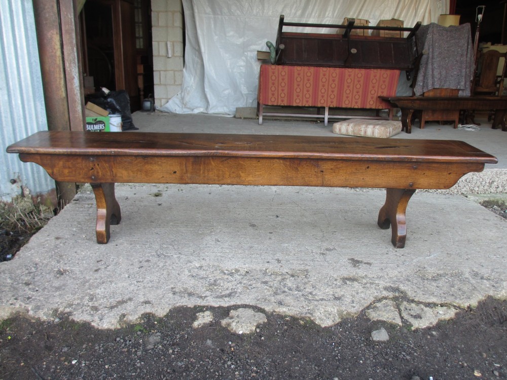 A long Edwardian solid oak bench featuring a rectangular seat and shaped trestle end supports. View V