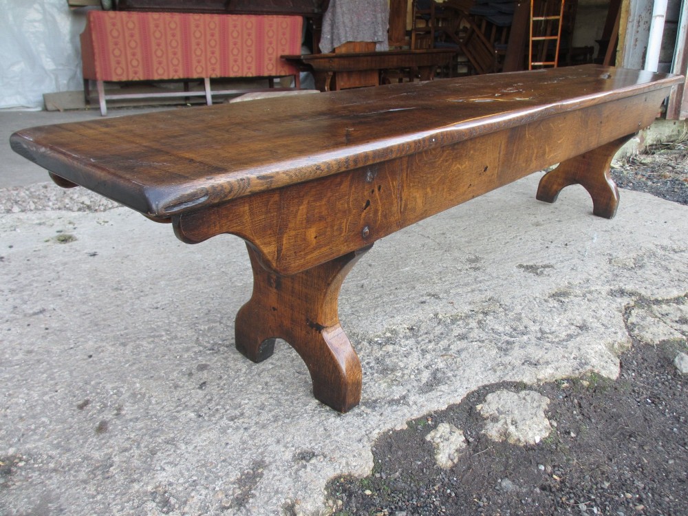A long Edwardian solid oak bench featuring a rectangular seat and shaped trestle end supports. View VI