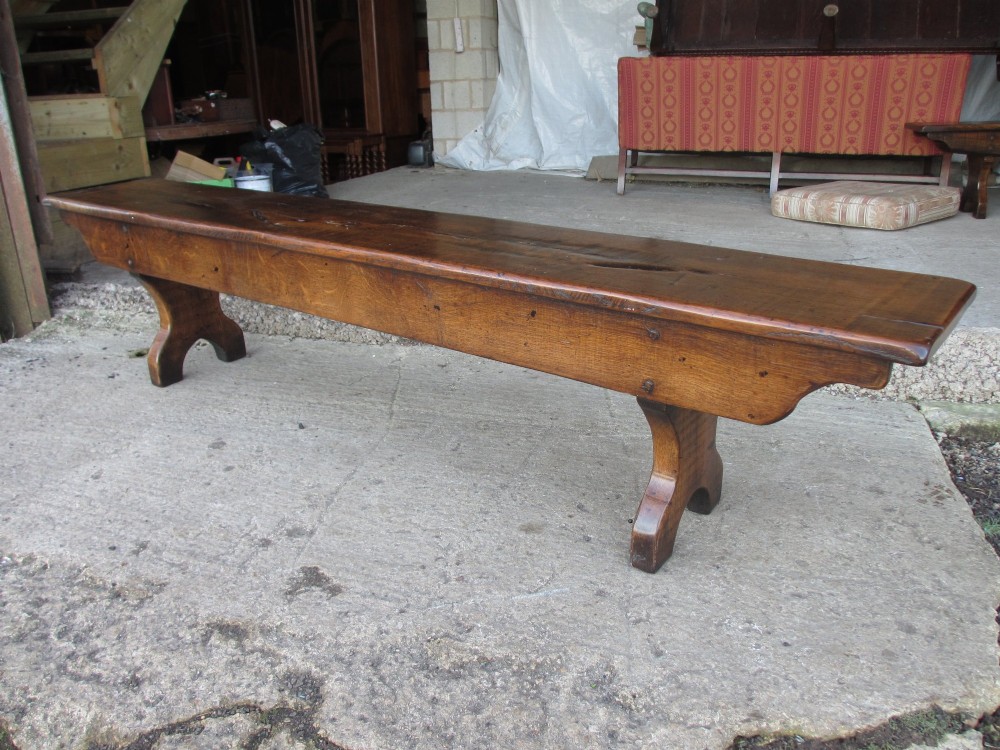 A long Edwardian solid oak bench featuring a rectangular seat and shaped trestle end supports. View VII