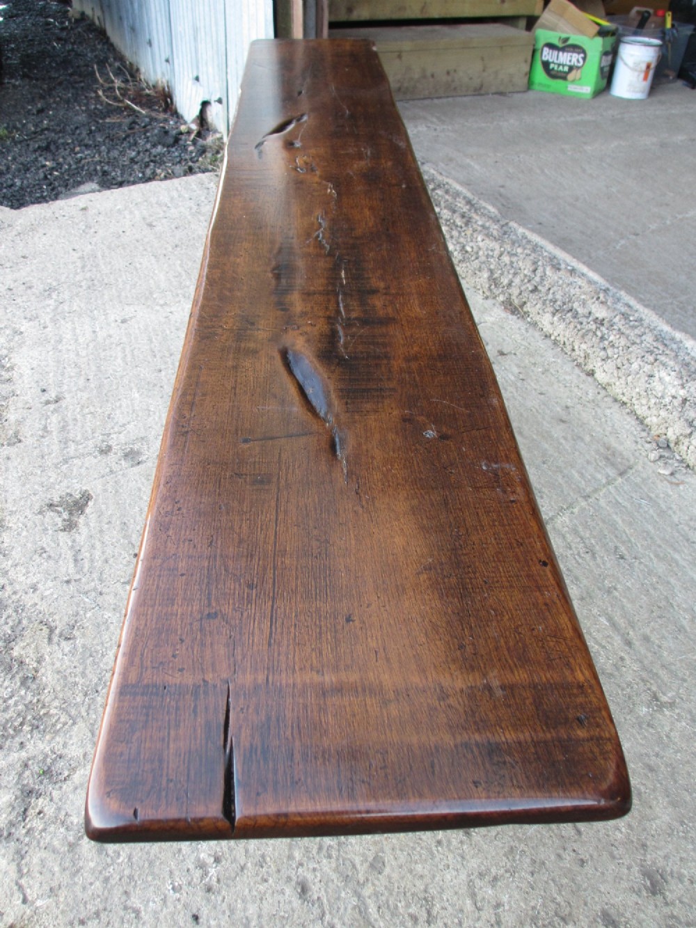 A long Edwardian solid oak bench featuring a rectangular seat and shaped trestle end supports. View VIII