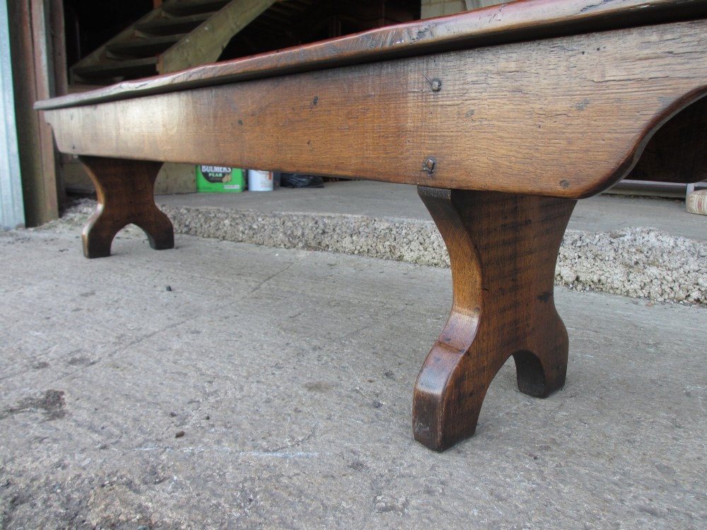 A long Edwardian solid oak bench featuring a rectangular seat and shaped trestle end supports. View XI