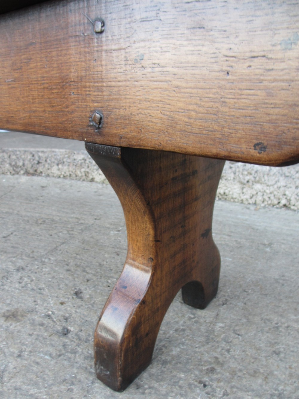 A long Edwardian solid oak bench featuring a rectangular seat and shaped trestle end supports. View XII