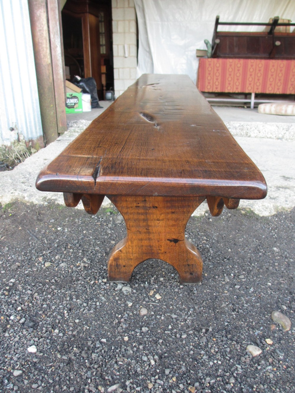 A long Edwardian solid oak bench featuring a rectangular seat and shaped trestle end supports. View XIV