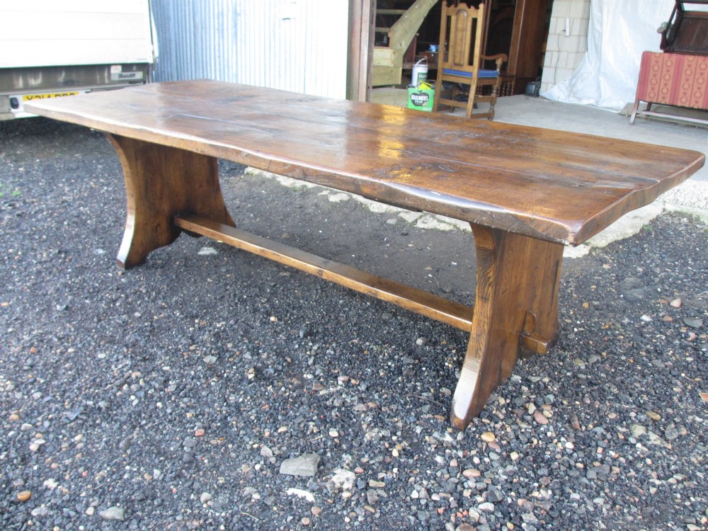 A solid oak refectory dining table featuring a thick plank top, shaped trestle ends, and a low central stretcher. View III