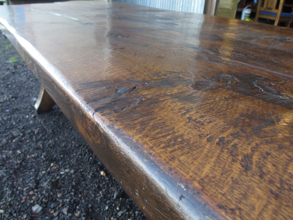 A solid oak refectory dining table featuring a thick plank top, shaped trestle ends, and a low central stretcher. View VI