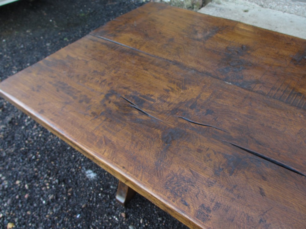 A solid oak refectory dining table featuring a thick plank top, shaped trestle ends, and a low central stretcher. View VII