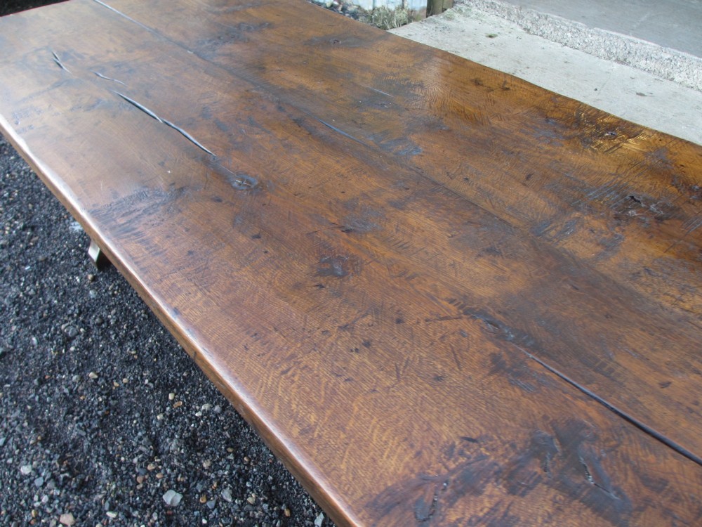 A solid oak refectory dining table featuring a thick plank top, shaped trestle ends, and a low central stretcher. View VIII