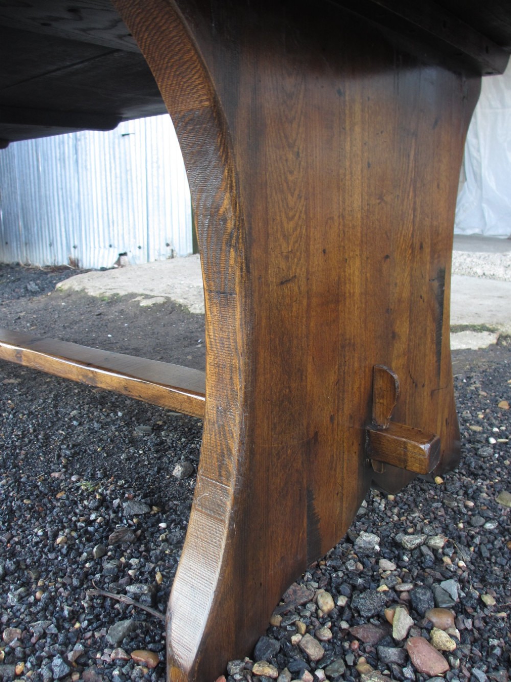 A solid oak refectory dining table featuring a thick plank top, shaped trestle ends, and a low central stretcher. View XI