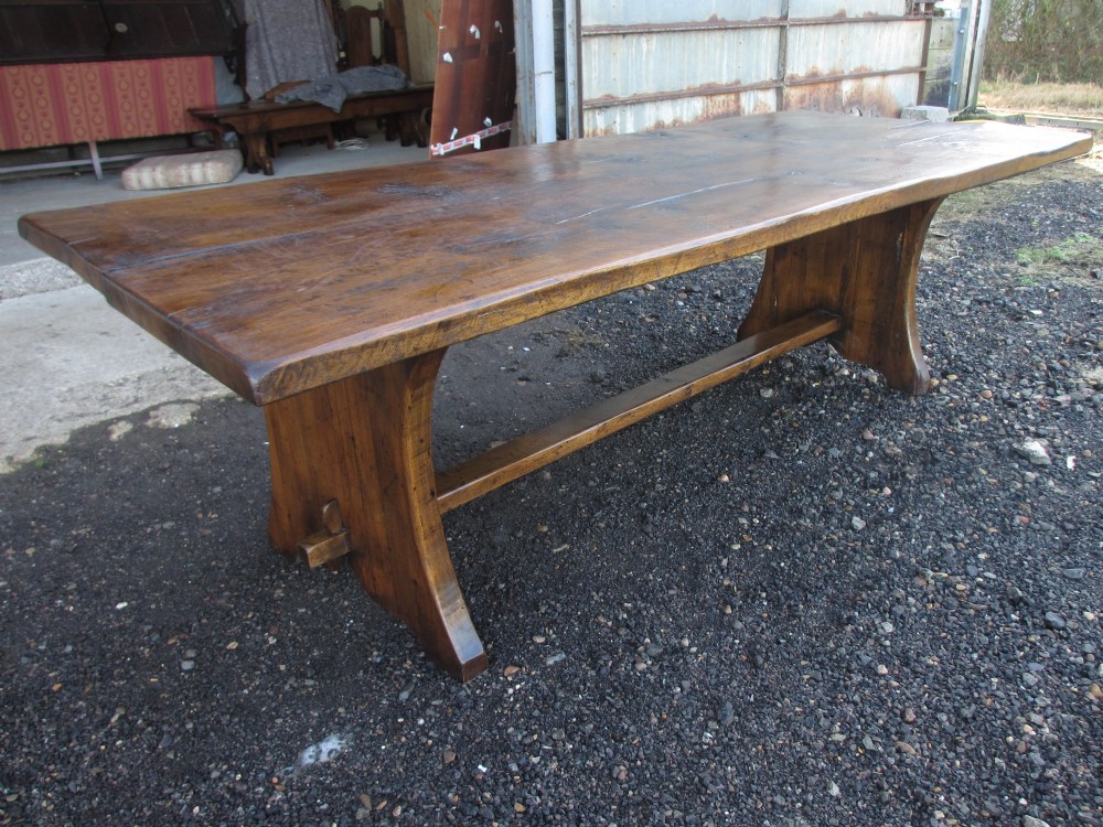 A solid oak refectory dining table featuring a thick plank top, shaped trestle ends, and a low central stretcher. View XIII