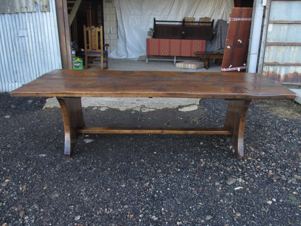 A solid oak refectory dining table featuring a thick plank top, shaped trestle ends, and a low central stretcher. View XIV