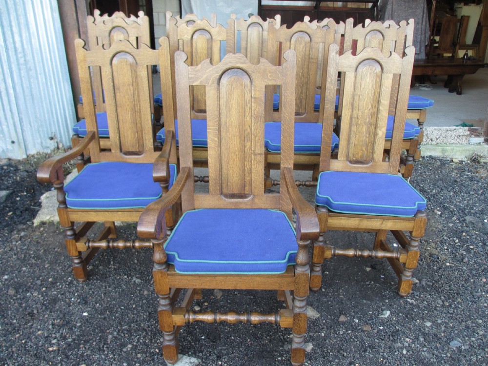 A set of twelve 20th-century oak high-back dining chairs with arched panel backrests and blue upholstered seat pads. View VI