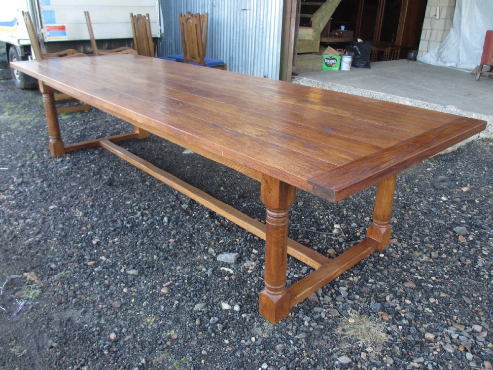 An eleven-foot oak refectory dining table with a planked top, low stretcher base, and heavy turned legs.