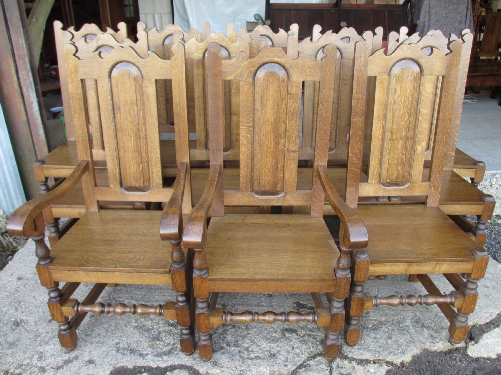 A long twentieth-century oak refectory dining table with turned legs and stretcher base, accompanied by twelve high-backed carved oak dining chairs with blue seat cushions. View XVI