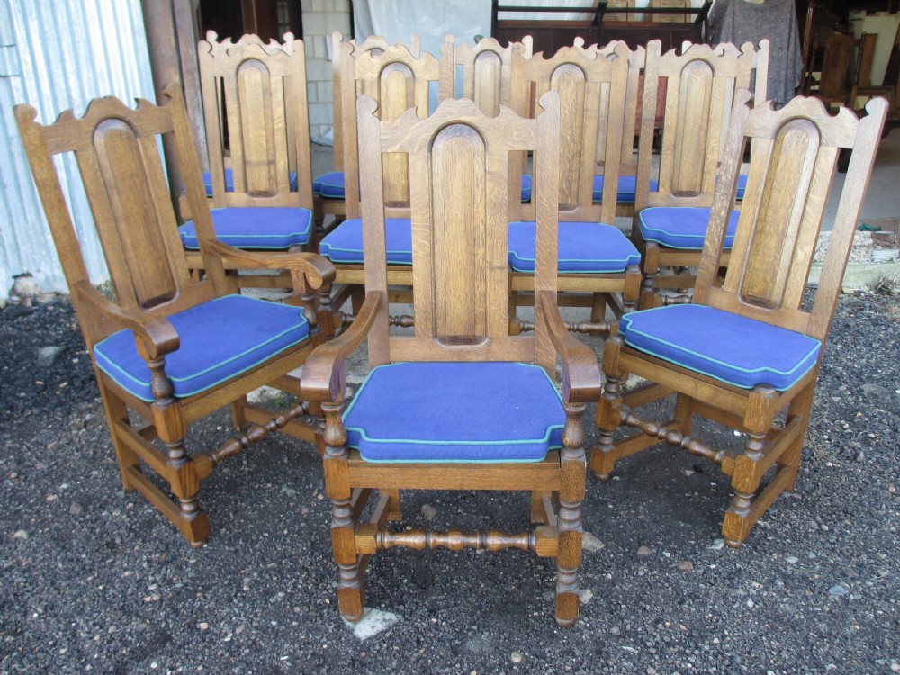 A long twentieth-century oak refectory dining table with turned legs and stretcher base, accompanied by twelve high-backed carved oak dining chairs with blue seat cushions. View II