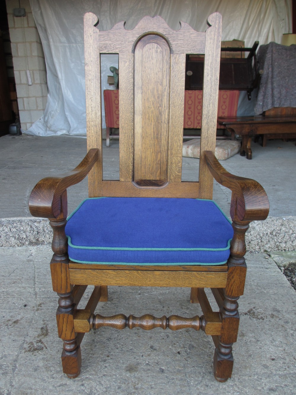 A long twentieth-century oak refectory dining table with turned legs and stretcher base, accompanied by twelve high-backed carved oak dining chairs with blue seat cushions. View III
