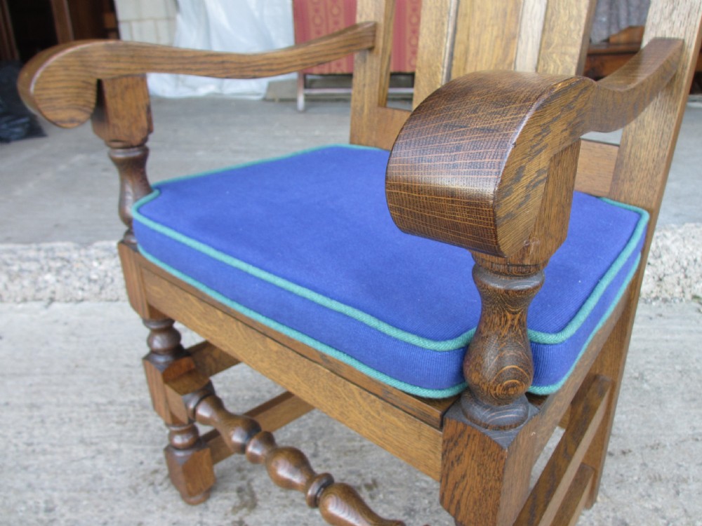 A long twentieth-century oak refectory dining table with turned legs and stretcher base, accompanied by twelve high-backed carved oak dining chairs with blue seat cushions. View IV