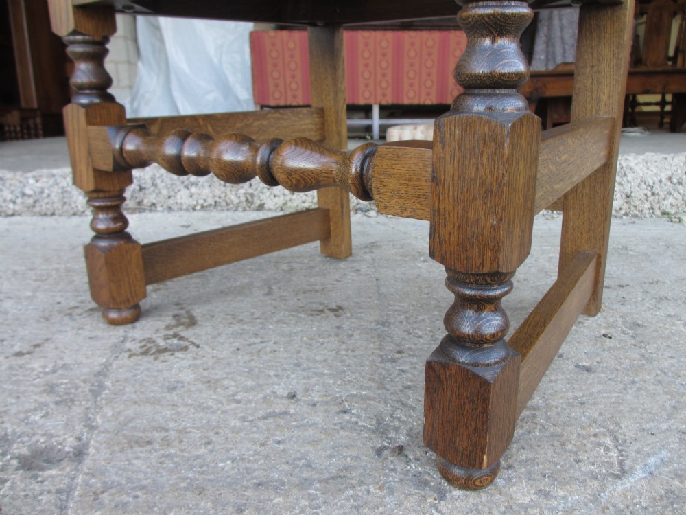 A long twentieth-century oak refectory dining table with turned legs and stretcher base, accompanied by twelve high-backed carved oak dining chairs with blue seat cushions. View V
