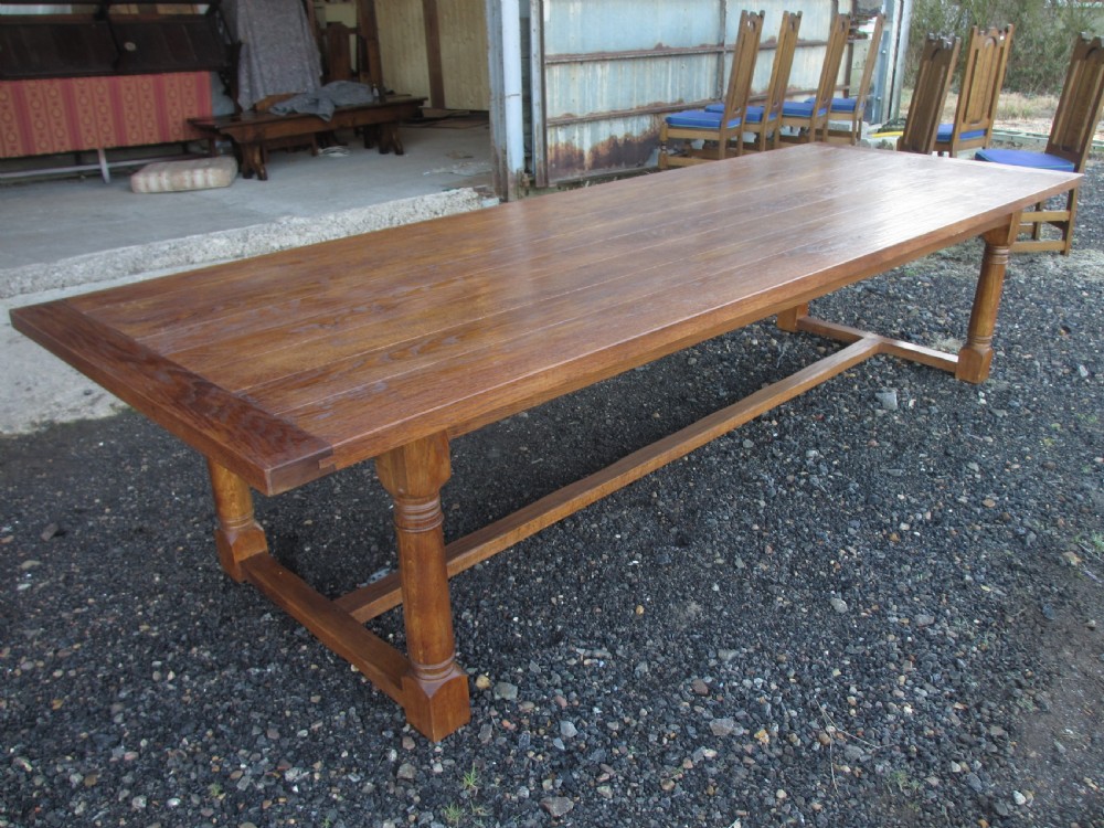 A long twentieth-century oak refectory dining table with turned legs and stretcher base, accompanied by twelve high-backed carved oak dining chairs with blue seat cushions. View XI