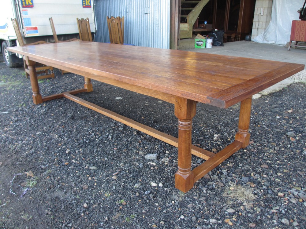 A long twentieth-century oak refectory dining table with turned legs and stretcher base, accompanied by twelve high-backed carved oak dining chairs with blue seat cushions. View XII