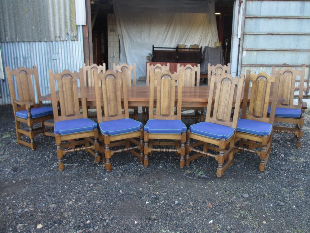 A long twentieth-century oak refectory dining table with turned legs and stretcher base, accompanied by twelve high-backed carved oak dining chairs with blue seat cushions. View XV