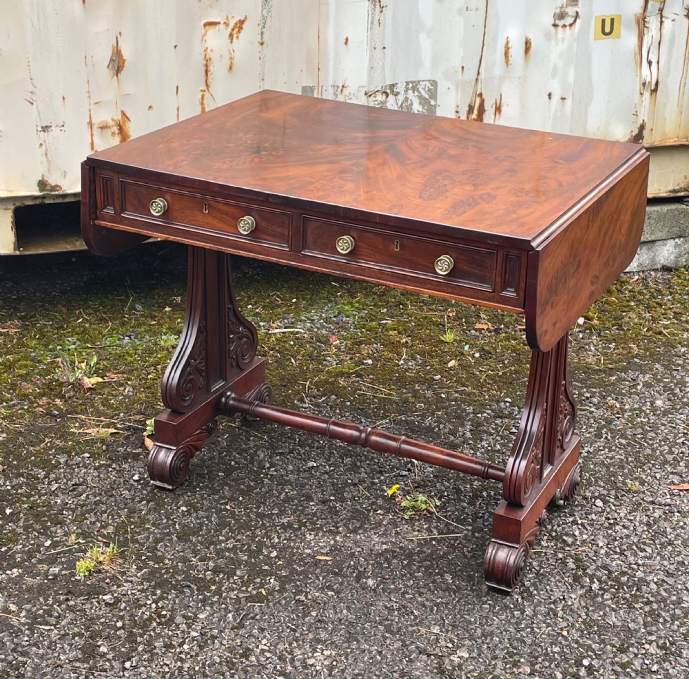 A William IV mahogany sofa table with two drop-leaf ends, frieze drawers with round brass knobs, and carved scroll trestle supports.